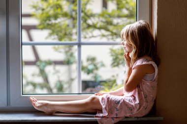 Pencerenin kenarında oturan sevimli küçük kız. Anaokulu çocuğu bakıyor ve rüya görüyor.