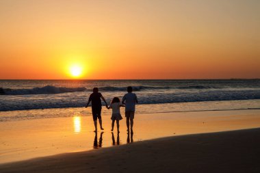 Gün batımında plajda koşup zıplayan üç çocuk silueti. Mutlu bir aile, iki okul çocuğu ve küçük bir anaokulu kızı. Kardeşler birlikte eğleniyor. Bağ kurmak ve aile tatili