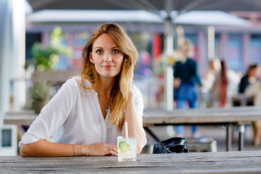 Genç bir kadın sıcak yaz gününde kafedeki terasta mojito kokteyli içiyor. Güzel bir iş kadını işten sonra restoranda sıcak bir akşam geçiriyor. Mutlu yalnız gülümseme bayan.