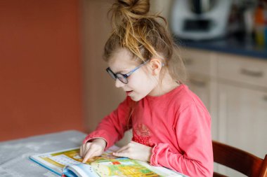 Gözlüklü küçük kız okumayı öğreniyor. İlkokulun çocuğu evde bir kitap okuyor, okul ödevi yapıyor.