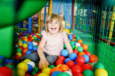 Kapalı alanda oynayan aktif küçük bir kız. Neşeli anaokulu çocukları tırmanıyor, koşuyor, zıplıyor ve renkli plastik toplarla eğleniyor. Çocuklar için kapalı etkinlik