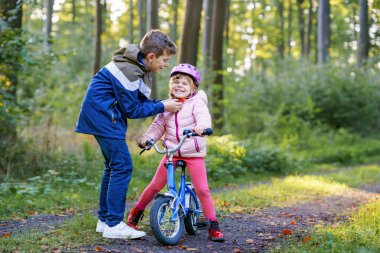Erkek kardeş, kız kardeş, kız kardeş bisiklet kaskını kafasına taktı. Kardeş mutlu çocuk bisikleti öğretiyor ve bisikletle eğleniyor. Aktif aile fertleri açık havada. Çocuk aktivitesi.