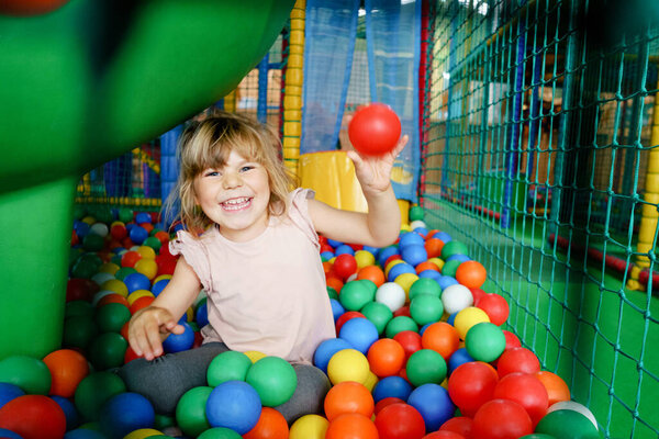 Active little girl playing in indoor playground. Happy joyful preschool child climbing, running, jumping and having fun with colorful plastic balls. Indoors activity for children
