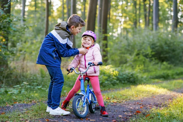 Erkek kardeş, kız kardeş, kız kardeş bisiklet kaskını kafasına taktı. Kardeş mutlu çocuk bisikleti öğretiyor ve bisikletle eğleniyor. Aktif aile fertleri açık havada. Çocuk aktivitesi.