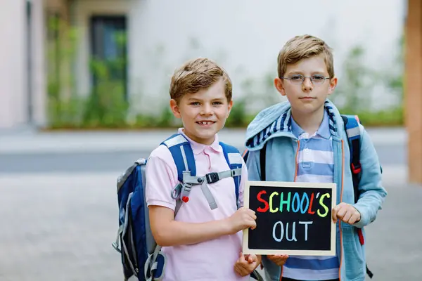 Two little kid boys with backpack or satchel. Schoolkids on the way to school. Healthy children, brothers and best friends outdoors on street leaving home. Schools out on chalk desk. Happy siblings