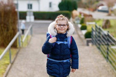 Okula giderken çok tatlı bir kızdı. İlkokula giderken gözlüklü sağlıklı ve mutlu bir çocuk. Okul çantalı gülümseyen çocuk şehir sokaklarında, açık havada. Okula geri dön.