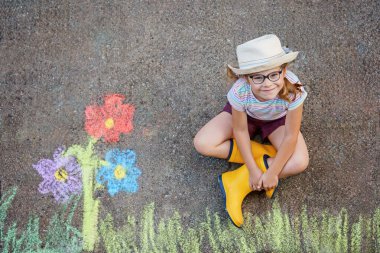 Sevimli küçük kız ve asfalta renkli tebeşirle boyanmış çiçekler. Mutlu anaokulu çocuğu tebeşirle resim yaparken eğleniyor. Çocuklar için yaratıcı eğlence, çizim ve resim