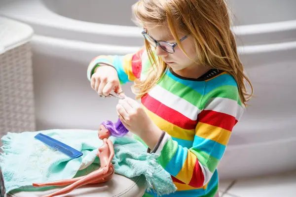 可爱的小女孩在家里玩洋娃娃 戴眼镜的孩子正在给她的玩具娃娃理发 为儿童开展的室内创作活动 — 图库照片