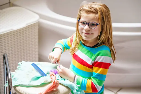 可爱的小女孩在家里玩洋娃娃 戴眼镜的孩子正在给她的玩具娃娃理发 为儿童开展的室内创作活动 — 图库照片