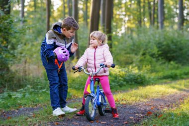 Erkek kardeş, kız kardeş, kız kardeş bisiklet kaskını kafasına taktı. Kardeş mutlu çocuk bisikleti öğretiyor ve bisikletle eğleniyor. Aktif aile fertleri açık havada. Çocuk aktivitesi.