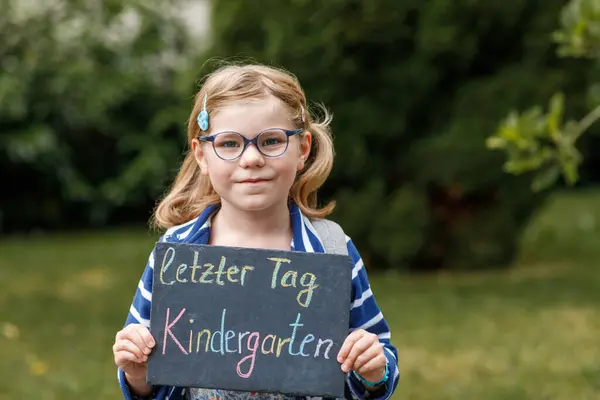 快乐的小女孩手里拿着黑板站在那里 幼儿园的最后一天是德语 在绿地公园 健康的学龄前儿童在户外戴着眼镜 — 图库照片