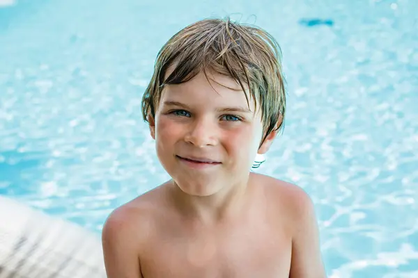 描述一个快乐的小男孩在游泳池边休息 在酒店度假胜地享受家庭度假的情景 健康的孩子在水里玩耍 游泳和泼水 图库照片