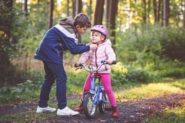 Erkek kardeş, kız kardeş, kız kardeş bisiklet kaskını kafasına taktı. Kardeş mutlu çocuk bisikleti öğretiyor ve bisikletle eğleniyor. Aktif aile fertleri açık havada. Çocuk aktivitesi.