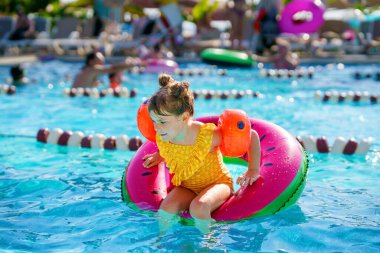 Şişme oyuncak yüzüklü mutlu küçük kız yüzme havuzunda yüzüyor. Küçük bir anaokulu çocuğu yüzmeyi ve otelin havuzuna dalmayı öğreniyor. Çocuklar için sağlıklı spor aktivitesi ve eğlence