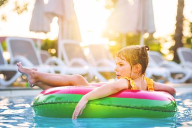 Şişme oyuncak yüzüklü mutlu küçük kız yüzme havuzunda yüzüyor. Küçük bir anaokulu çocuğu yüzmeyi ve otelin havuzuna dalmayı öğreniyor. Çocuklar için sağlıklı spor aktivitesi ve eğlence