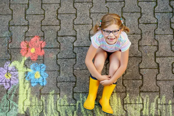 かわいい少女とアスファルトにカラフルなシャークで描かれた花 絵画チョークの絵で楽しんでいる幸せな幼稚園児 絵画のためのクリエイティブなレジャー ストック画像
