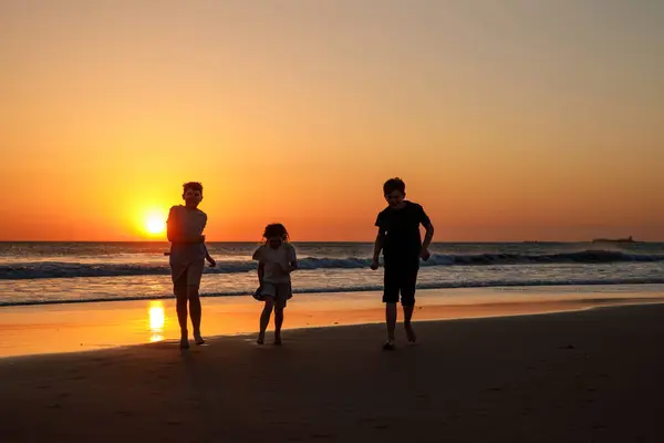 Три Детских Силуэта Бегают Прыгают Пляже Закате Счастливая Семья Двое — стоковое фото