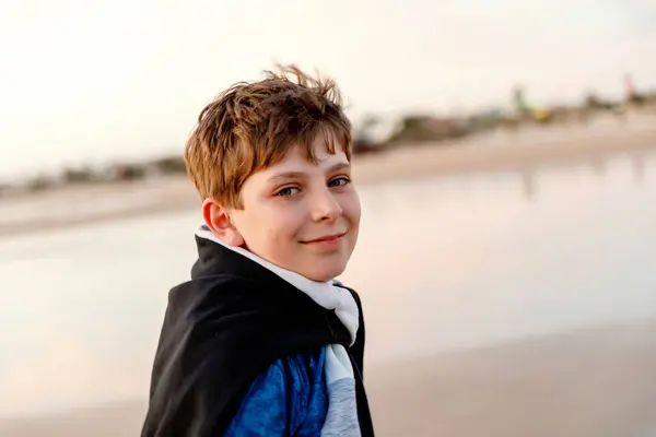 日落时站在海滩上快乐快乐的少年 快乐的十多岁男孩在镜头前笑着 孩子们在海上度假 图库图片