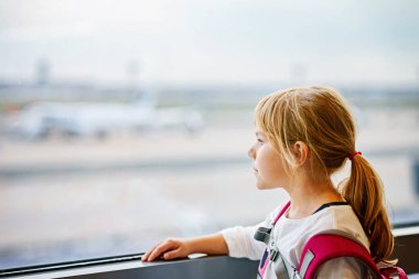 Küçük kız havaalanında Büyük Pencere 'de pansiyon bekliyor. Şirin Çocuk Pencere 'de, uçakların arka planına karşı duruyor. Aile Yaz tatili için ayrılmayı dört gözle bekliyorum..
