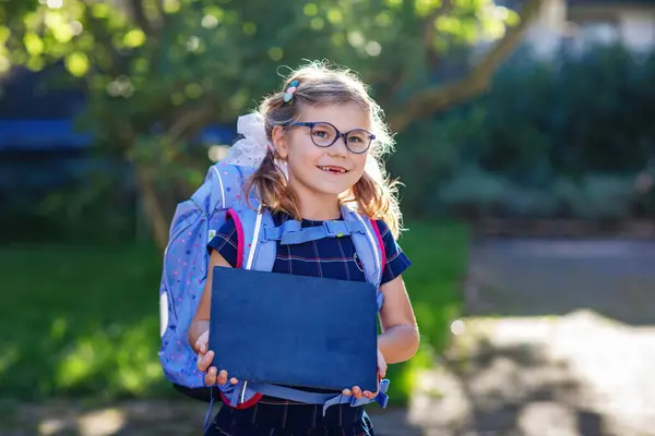 开学第一天 快乐的小女孩 戴着眼镜 背着背包或书包 背着大书包 健康可爱的孩子在户外 第一天上学时 孩子们都拿着粉笔 — 图库照片