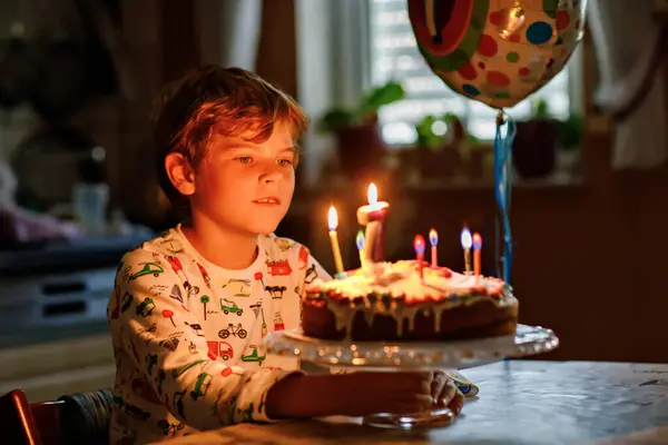可爱的金发小男孩庆祝他的生日 小孩在自家做的烤蛋糕上吹了7支蜡烛 在室内 学生生日聚会 7周年家庭庆祝活动 图库照片
