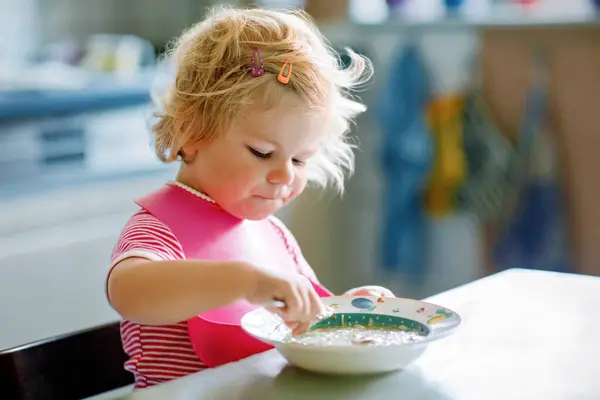 可爱的女婴吃着勺子蔬菜面汤 健康食品 喂养和发展概念 可爱的小孩 带着勺子坐在高椅子上 学习自己吃饭 图库照片