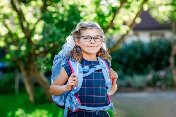 バックパックまたはサテラスと学校の最初の日に大きなスクールバッグで眼鏡をかけた幸せな小さな少女 屋外で健康な愛らしい子供たち 学校に戻る ストックフォト