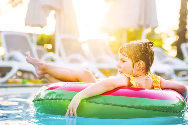 膨脹可能なおもちゃのリングが付いている幸せな少女はプールで浮きます リトルプリスクールの子供は ホテルリゾートの屋外プールで泳ぎ ダイビングを学びます 健康的なスポーツアクティビティと子供のための楽しい ストックフォト