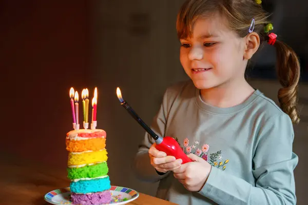 誕生日を祝う幸せな小さな就学前の女の子 手作りの虹のケーキ 屋内でかわいい笑顔の子供 幸せな健康な幼児吹いて6キャンドルオンケーキ ストック写真