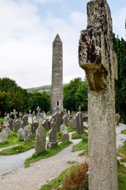 Taş yuvarlak kule ve bir manastır yerleşim bazı kalıntıları aslında Glendalough vadisinde 6 yüzyılda inşa, County Wicklow, İrlanda güneşli bir günde.