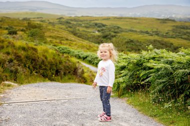 Cute little happy toddler girl running on nature path in Connemara national park in Ireland. Smiling and laughing baby child having fun spending family vacations in nature. Traveling with small kids. clipart