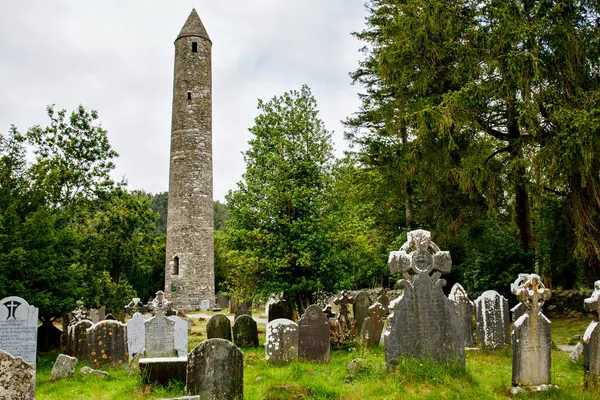 石头圆塔和一些废墟的修道院定居点最初建于6世纪格伦达洛山谷 威克洛县 爱尔兰在阳光明媚的日子 图库照片