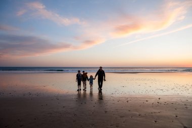 Gün batımında üç çocuk ve babanın resimli mutlu çocukları ve babaları sahilde. Mutlu bir aile, iki okul çocuğu ve küçük bir anaokulu kızı. Kardeşler birlikte eğleniyor. Bağlanma.