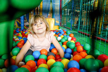 Kapalı alanda oynayan aktif küçük bir kız. Neşeli anaokulu çocukları tırmanıyor, koşuyor, zıplıyor ve renkli plastik toplarla eğleniyor. Çocuklar için kapalı etkinlik
