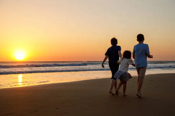 Drei Kinder Rennen Und Springen Bei Sonnenuntergang Strand Glückliche Familie lizenzfreie Stockfotos