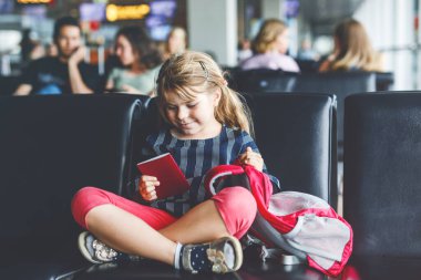 Küçük kız havaalanında büyük pencerede biniş için bekliyor. Pasaportu olan sevimli bir çocuk yaz tatiline gitmeyi dört gözle bekliyor..