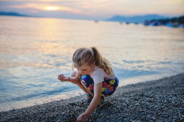 Küçük kız güzel bir okyanus sahilinde yürüyor. Deniz sahilinde günbatımında mutlu anaokulu çocukları oynuyor. Yazın çocuklarla aile tatilleri
