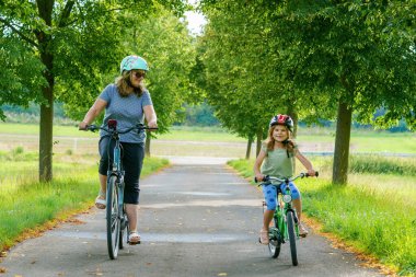 Mutlu aile dışarıda bisiklet sürüyor ve gülümsüyor. Anne ve kız, bisiklet süren küçük tatlı okul öncesi kız, aktif eğlence ve spor birlikte.