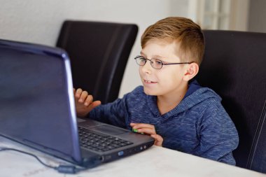 Gözlüklü sağlıklı çocuk evde defteriyle ödev yapıyor. İnternetin yardımıyla ilgili bir çocuk kompozisyon yazıyor. konsept okul çocukları kavramı.