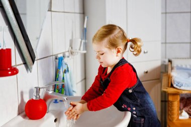 Küçük tatlı kız banyoda sabun ve suyla ellerini yıkıyor. Sevimli çocuk vücut parçalarını temizlemeyi öğreniyor. Sabah hijyen rutini. Evde ya da kreşte mutlu sağlıklı bir çocuk