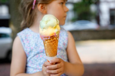 Güneşli yaz gününde krep külahında dondurma yiyen küçük bir anaokulu kızı. Mutlu çocuk dondurma tatlısı yesin. Sıcak yaz günlerinde tatlı yiyecekler. Parlak ışık, renkli dondurma..