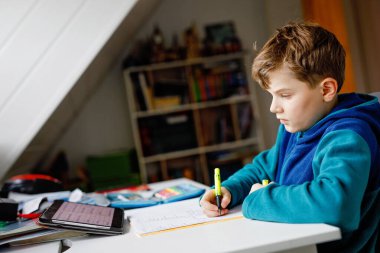 Okul çocuğu evde okul için tabletle öğreniyor. Ev ödevi yapan, ped kullanan ve modern aletler kullanan sevimli bir çocuk. Evde eğitim ve uzaklık öğrenme kavramı