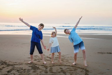 Üç çocuk, gün batımında okyanus sahilinde mutlu kardeşler. Mutlu bir aile, iki okul çocuğu ve küçük bir anaokulu kızı. Kardeşler eğleniyor, İspanya, Costa del Sol