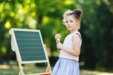 Mutlu küçük çocuk kız büyük tebeşir masa okul öncesi veya temel tarafından İlköğretim okulun ilk günü ayakta. Geri okul kavramı. Yazma ve açık havada resim sağlıklı çocuk. Boşaltmak üstünde okul sırası
