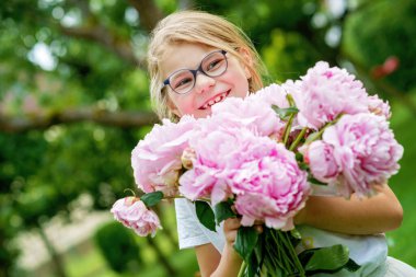 Doğanın arka planında çiçek açmış, el ele tutuşan, koklayan ve bir buket pembe şakayık çiçeğinin tadını çıkaran, mutlu, küçük beyaz bir kız çocuğunun portresi.
