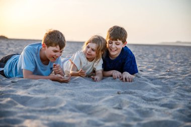 Üç çocuk gün batımı okyanus sahilinde kumla oynuyor. Mutlu bir aile, iki okul çocuğu ve küçük bir anaokulu kızı. Kardeşler birlikte eğleniyor. İspanya, Endülüs 'te aile tatili.