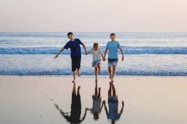 Üç çocuk, gün batımında okyanus sahilinde mutlu kardeşler. Mutlu bir aile, iki okul çocuğu ve küçük bir anaokulu kızı. Kardeşler eğleniyor, İspanya, Costa del Sol