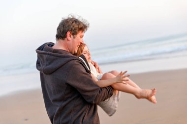 Sağlıklı bir baba ve kızı gün batımında kumsalda birlikte oynuyorlar. Mutlu bir aile, aşkım. Anaokulu kızı ve orta yaşlı adamın kucaklaşması. Ebeveynler ve çocuklar arasında mutlu bir ilişki