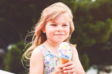 Güneşli yaz gününde krep külahında renkli dondurma yiyen mutlu anaokulu kızı. Küçük çocuk dondurmalı tatlı yiyordu. Sıcak yaz günlerinde tatlı yiyecekler. Parlak ışık, renkli dondurma..