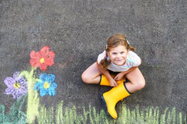 Sevimli küçük kız ve asfalta renkli tebeşirle boyanmış çiçekler. Mutlu anaokulu çocuğu tebeşirle resim yaparken eğleniyor. Çocuklar için yaratıcı eğlence, çizim ve resim